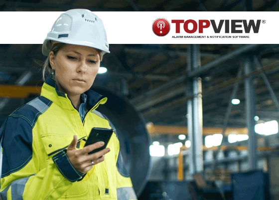 Engineer in safety gear using TopView alarm management and notification software on a mobile device inside an industrial facility for remote monitoring.